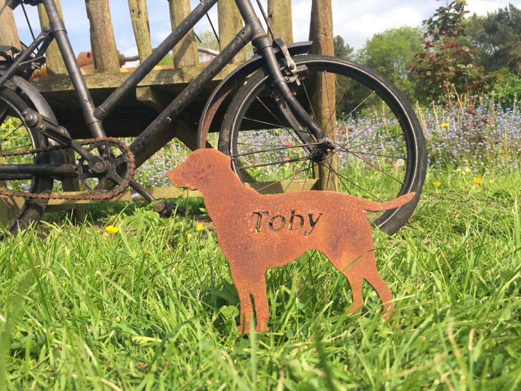 A hand-cut steel memorial marker engraved with the name Toby, in a garden